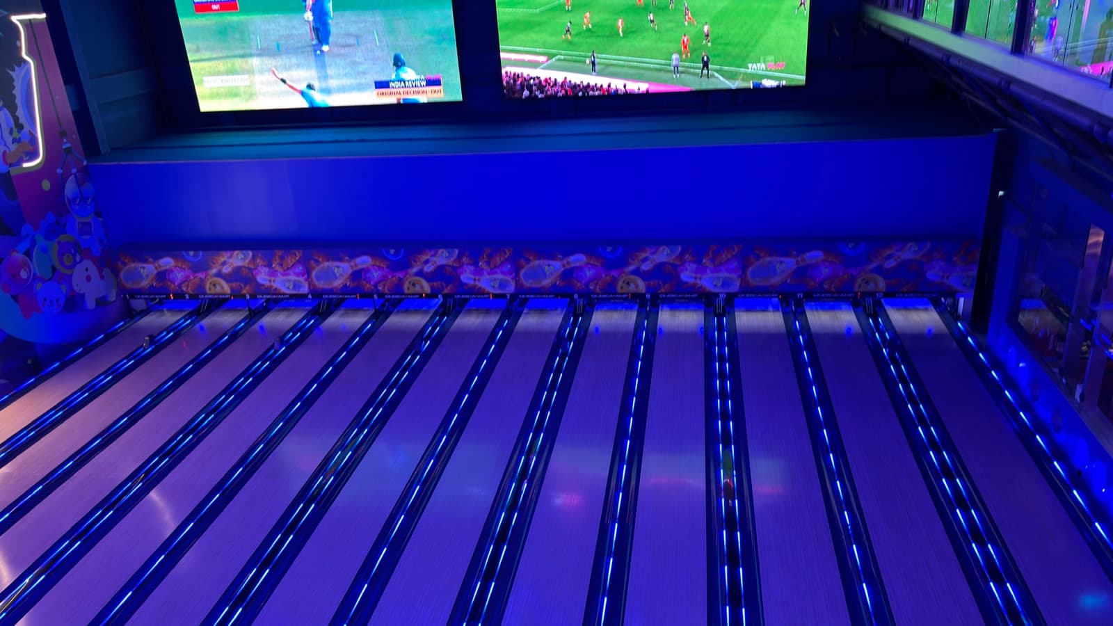 Blue-lit bowling lanes with football on screens